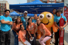 Smiling young adults in blue and orange shirts pose with a goldfish mascot.