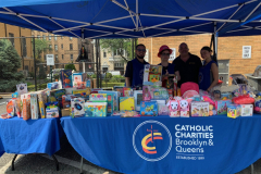 A group of smiling adults stands behind a table full of toys at an outdoor event.