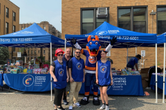 Four smiling adults pose with a blue and orange dragon mascot wearing a New York Islanders uniform at an outdoor event.