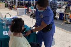 A woman is sitting in a chair having her blood pressure taken by a woman in a blue uniform.
